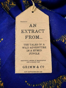 Image of the story extract scarf 'Extract from a tale in the jungle (tiger)' with a printed pattern of yellow tigers with dark blue stripes set on a background of royal blue. Kraft paper label is shown with description 'An extract from the tales of a wild adventure in a humid jungle'.