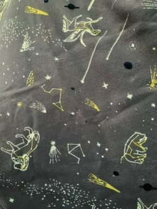 Image of the story extract scarf 'Extract from a tale of heroes' with a printed pattern of zodiac constellations such as pegasus and little bear among shooting stars and distant planets in white and yellow on a background of lilac-grey. Image shows detail of full printed fabric.