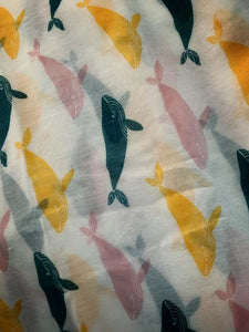 Image of the story extract scarf 'Extract from tales with whales' with a printed repeating pattern of yellow, teal and pale pink whales on a white background. Image shows detail of full printed pattern.