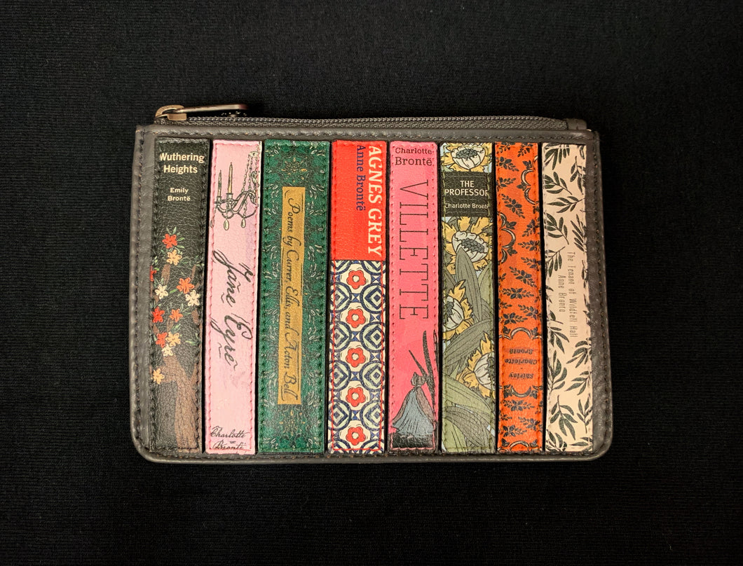 Image shows the Yoshi Coin Keeper purse featuring book titles by the Bronte Sisters. Purse is a dark grey leather and a zip across the top.
