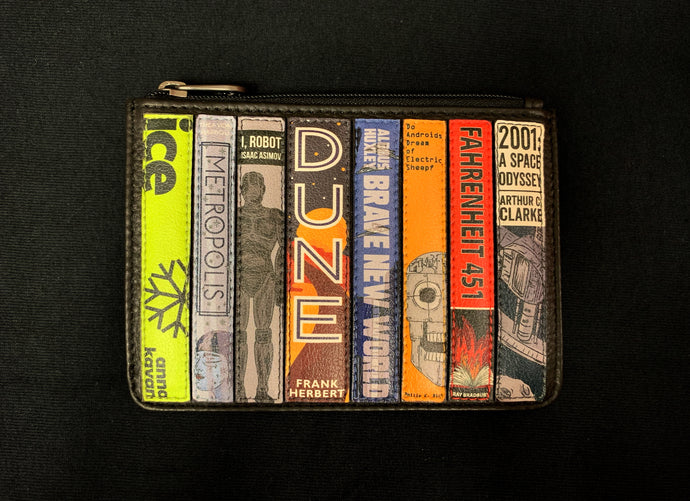 Image shows the Yoshi leather coin keeper featuring appliqued leather book spines in various colours and designs of Sci-Fi novels. Titles include Dune, I, Robot and Fahrenheit 451. Purse is black leather with a zipper across the top. 