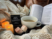 Load image into Gallery viewer, Image showing a white blanket on a brown sofa with an open book and a tray holding two battery operated candles, a cup of coffee and a mini bowl containing two wax melts and the Cosy Book Nook Scent Portal sat next to them.