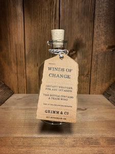 Image of the Winds of Change bottle from the Airs and Graces range: An empty glass potion bottle with cork. The bottle has a kraft tag around the neck, reading: Winds of Change.  Instant weather for any occasion. This bottle contains a trade wind