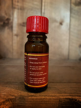 Load image into Gallery viewer, Image of the Christmas in a Bottle scented oil. Bottle is brown glass with a red top and label. Image shows the warning label - keep away from children, do not use internally or apply to skin, do not place onto polished wooden surface, if in contact with eyes, rinse with water and seek medical attention.