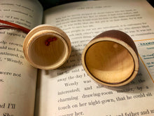 Load image into Gallery viewer, Image shows A Kiss wooden acorn-shaped bauble in two halves displayed open to show the hollowed out inside with space to store messages, trinkets and small gifts. Acorn sat on open pages of the book of Peter Pan.