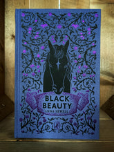 Load image into Gallery viewer, Image of the front cover of the Puffin clothbound classic Black Beauty with a purple background and a close-up print of a black horse and rose thorns with purple foiled roses and buds in a mirrored pattern.