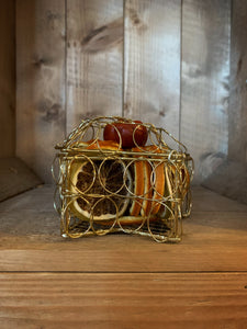 Side on view image of Scent of the Season Star Centrepiece sat flat on a surface, a gold wire box in the shape of a star filled with pot pourri including dried orange and green orange slices and a dried mini pumpkin