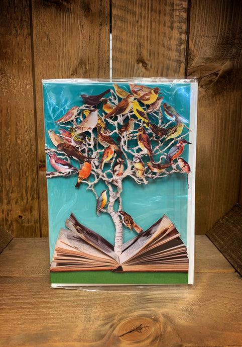 Image of an A5 laser cut greetings card with a turquoise background (inside the card). The card has a laser cut tree coming up from the centre pages of an open book and nestled in the tree are all different kinds of birds in the branches.