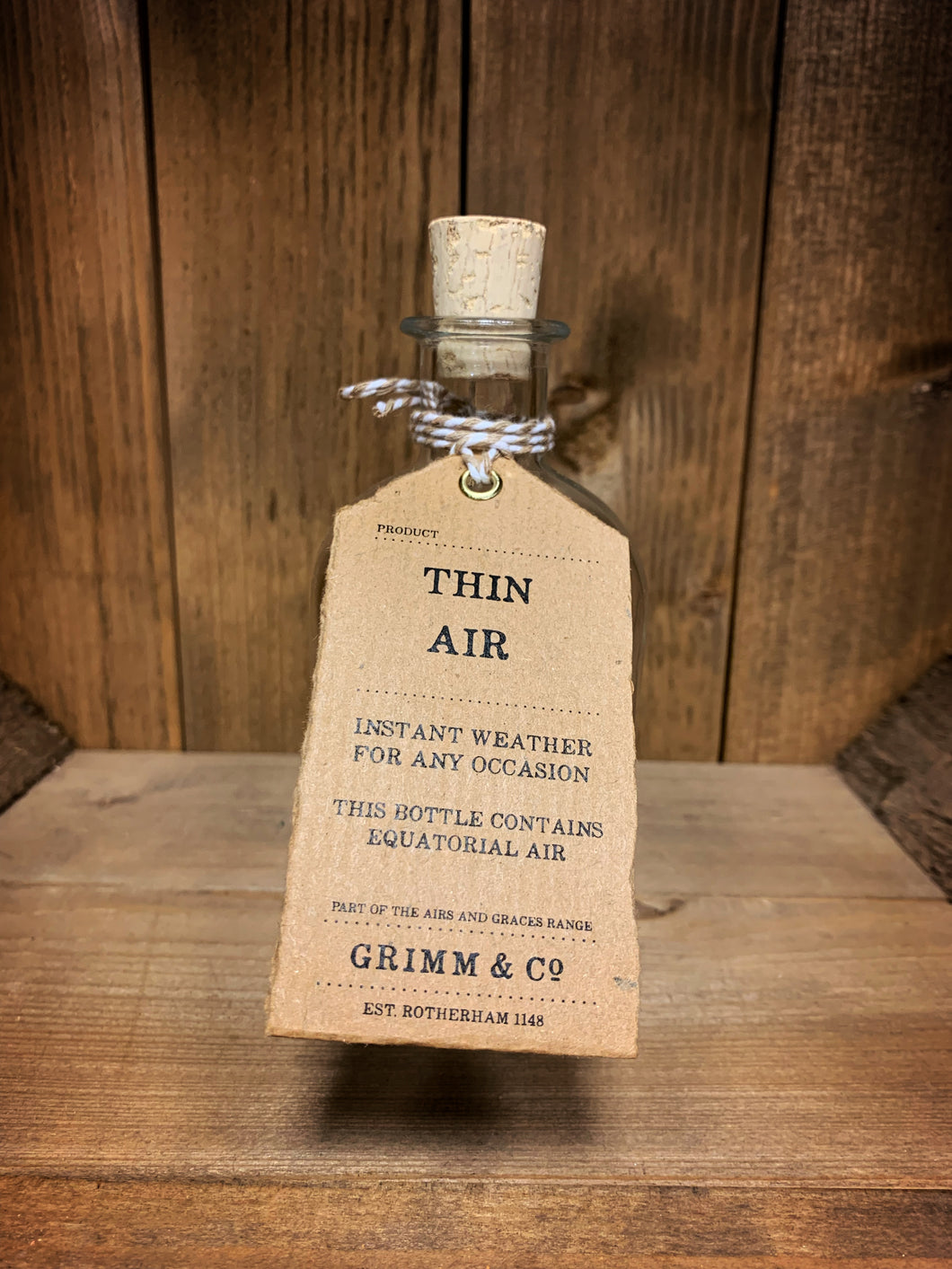 Image of the Thin Air  bottle from the Airs and Graces range: An empty glass potion bottle with cork. The bottle has a kraft tag around the neck, reading: Thin Air. Instant weather for any occasion. This bottle contains equatorial air