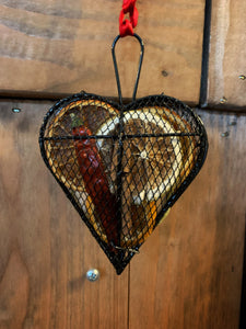 Image of the Scent of the Season Tree Decoration shaped as a heart. Decoration is a black wire shaped hanging box with hanging loop and ribbon. Box is filled with pot pourri including dried orange and green orange slices, a dried red chilli and cinnamon stick