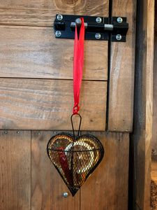 Image of the Scent of the Season Tree Decoration shaped as a heart. Decoration is a black wire shaped hanging box with hanging loop and ribbon. Box is filled with pot pourri including dried orange and green orange slices, a dried red chilli and cinnamon stick. Image shows the decoration hanging using the ribbon loop.