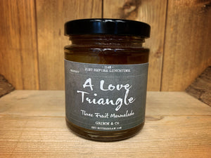 Image shows the front of the label for 'A Love Triangle' Marmalade (lemon, grapefruit, and orange). The small cylindrical jar has a dark, blackboard style label with white cursive text.