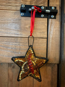 Image of the Scent of the Season Tree Decoration shaped as a star. Decoration is a black wire shaped hanging box with hanging loop and ribbon. Box is filled with pot pourri including dried orange and green orange slices, a dried red chilli and cinnamon stick. Image shows the decoration hanging using the red ribbon.