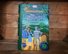 Load image into Gallery viewer, Image showing the book-shaped Jigsaw Library The Wonderful Wizard of Oz with a front cover design depicting Dorothy, Scarecrow, Tin Man and the Cowadrly Lion looking out across the yellow brick road to the Emerald City.