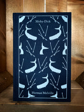 Load image into Gallery viewer, Image of the front cover of the Penguin clothbound classic Moby Dick featuring a navy blue background and a repeat pattern of pale grey whales whale tails with harpoons interspersed among them.