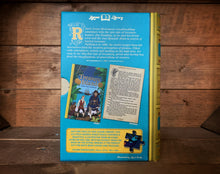 Load image into Gallery viewer, Image of the Jigsaw Library Treasure Island showing the back cover of the book-shaped box and the double-sided puzzle design with the image and an excerpt from the story.
