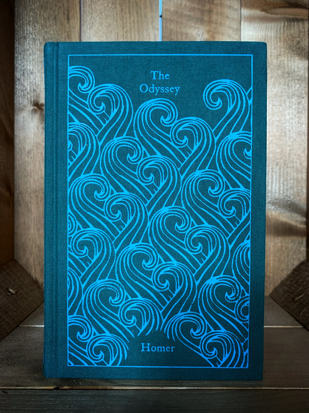 Image of the front cover of the Penguin clothbound classic The Odyssey featuring a teal background and a repeat pattern of printed light blue waves.