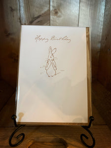 Image of the greetings card Beatrix Potter Peter Rabbit Birthday with a cream card and brown linear illustration of Peter Rabbit with the words 'Happy Birthday' across the top