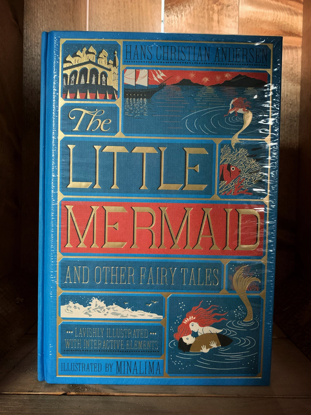Image of The Little Mermaid and Other Fairy Tales edition by MinaLima. This book features a bright blue clothbound cover wprinted with red, gold and dark blue to showcase images from the Little Mermaid. Images include the undersea castle, the mermaid above the sea watching a ship, a fish amongst coral and the little mermaid with the shipwrecked prince on the waves.