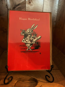 Image of greetings card Alice White Rabbit Birthday with a red background and a black and white illustration of the White Rabbit wearing a tabbard with red hearts and holding a bugle and scroll. The words 'Happy Birthday!' are written across the top