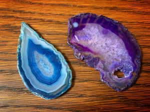 Image of two crystallized fairy wings, agate slices with tear-drop shapes, one blue and one purple slice with the appearance of coloured glass.