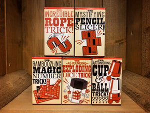 Image shows all five boxed magic tricks in a stack. On the bottom row there is the Magic Number Trick, the Exploding Dice Trick, and the Cup & Ball Trick. On the top row, there is the Rope Trick, and the Pencil Slicer. All the boxes have an illustration of the trick inside on the front.