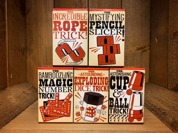 Image shows all five boxed magic tricks in a stack. On the bottom row there is the Magic Number Trick, the Exploding Dice Trick, and the Cup & Ball Trick. On the top row, there is the Rope Trick, and the Pencil Slicer. All the boxes have an illustration of the trick inside on the front.