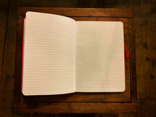 Load image into Gallery viewer, Image is of a Red Note Keeper laid out open, showing the lined pages. The likes on the page are slightly slimmer than a standard lined notebook. The elasticated pen holder can be clearly seen attached on the right side in the middle.