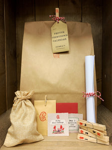 Image shows the packaged Festive Countdown Calendar. A kraft paper bag pegged shut with a kraft card label attached to the peg with red and white striped twine. In front of the bag are a few examples of what is inside. From left to right: a drawstring jute bag tied shut, a small kraft pouch containing the length of twine, a red envelope with two parts of the 24 day story writing challenge, 4 pegs in a stack that are labelled 1, 2, 3, and 4, and a scroll of white paper instructions tied with striped twine. 