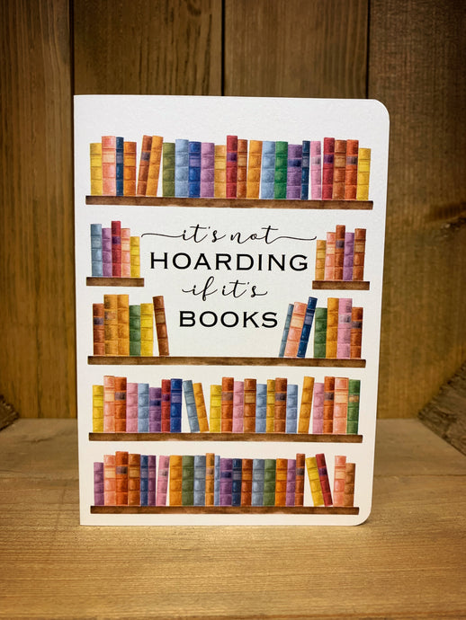 Images shows the front of the Book Hoarder card. It features a full-length illustration of a bookshelf and brightly coloured books, with 'It's not hoarding if it's books' written in the middle, in a mixture of bold print and cursive fonts. The design is printed on white pearlescent card.