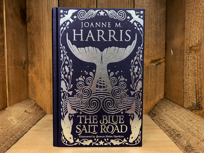 Image shows the front cover of the book The Blue Salt Road. The book is bound in navy coloured cloth, with the title, and flowing seaweed patterns and a fishtail illustration embossed in silver.