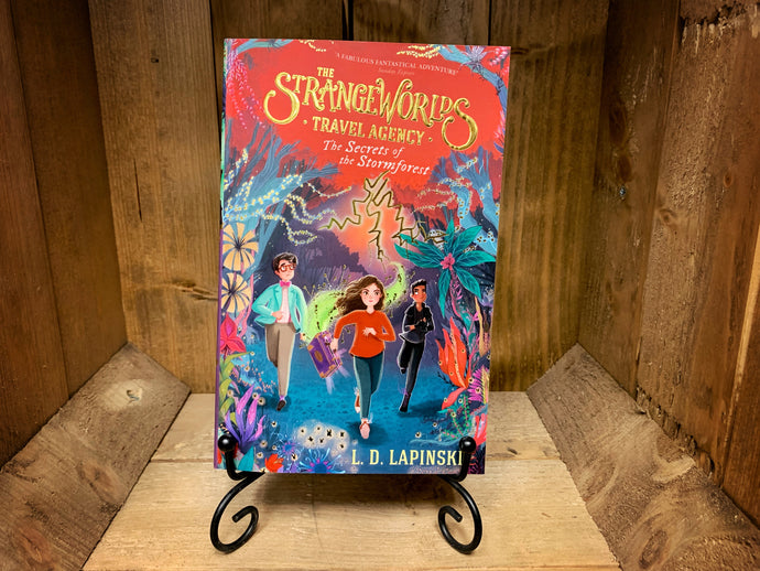 Image shows the front cover of the book The Strangeworlds Travel Agency: Secrets of the Stormforest. The cover has an illustration of three characters walking through a fantasy forest in  shades of blue, orange, purple, and red.