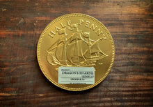 Load image into Gallery viewer, Image shows a single Dragon&#39;s Hoard chocolate coin - a giant chocolate coin with a gold &#39;half-penny&#39; embossed foil coating and a small kraft Grimm &amp; Co. product sticker on the lower half. 