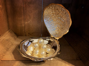 Image shows a small pile of cream-coloured bath pearls sitting inside a silver clam shell.