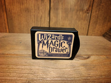 Load image into Gallery viewer, Image of the Magic Draw closed. It is a small, black box, with Wizard&#39;s Magic on the front, and a small lip at one end to pull out the draw.