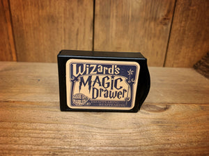 Image of the Magic Draw closed. It is a small, black box, with Wizard's Magic on the front, and a small lip at one end to pull out the draw.