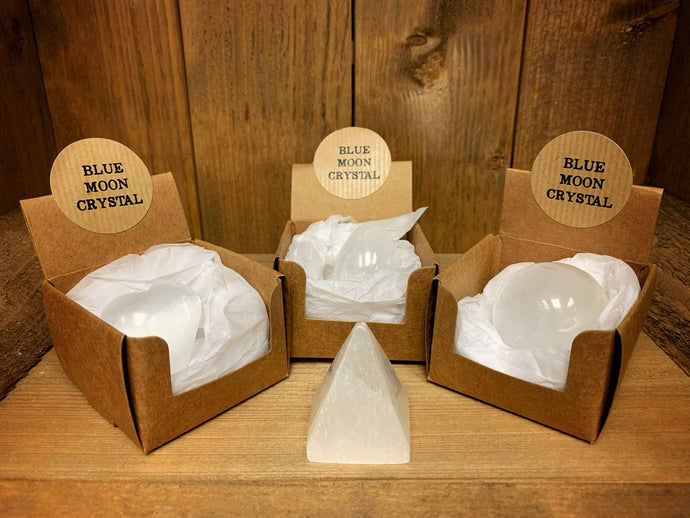 Image shows the four variant shapes of Blue Moon Crystal. Three of them are displayed in their brown kraft card gift boxes, with the pyramid version standing in front.