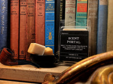 Load image into Gallery viewer, Image showing the Forgotten Library Scent Portal displayed against a backdrop of old clothbound books with a tobacco pipe sat on the bookshelf and a mini bowl containing two wax melt cubes.