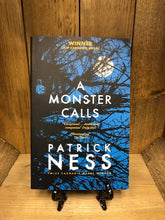 Load image into Gallery viewer, Image of the paperback book A Monster Calls by Patrick Ness,featuring a cover image of a blue night sky, a full, white moon and silhouetted tree branches.