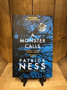 Image of the paperback book A Monster Calls by Patrick Ness,featuring a cover image of a blue night sky, a full, white moon and silhouetted tree branches.