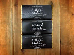 Image shows all three A Blissful Interlude chocolate bars in milk, white and dark. All packaging is the same with a black wraparound label and gold foil.